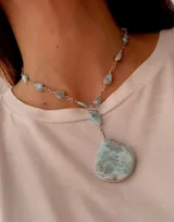 Collar de cadena de plata con engarces artesanales que sostienen pequeñas piedras naturales en tonos celeste y verde agua. Presenta un dije central de gran tamaño con forma orgánica y acabado irregular.