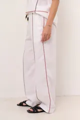 Pantalon de lino color marrón con costuras blancas decorativas a lo largo de las piernas y corte amplio.