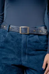 Cinto de cuero azul con hebilla metálica rectangular en tono bronce envejecido. Presenta detalles decorativos de tachas metálicas circulares y en forma de estrella a lo largo de la tira.