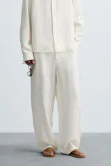 Pantalón de corte relajado confeccionado en tejido de cáñamo color blanco roto. Presenta cintura elástica con cordón interior ajustable, cierre frontal con botones, bolsillos laterales y un bolsillo trasero de plastrón.