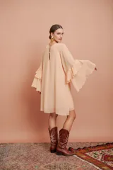 Vestido corto de manga larga acampanada con volados en cascada, color salmón claro, de corte suelto y escote redondo.