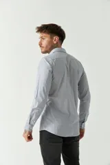 Camisa de hombre de corte slim fit, confeccionada en algodón con diseño de rayas verticales finas en tonos claros. Presenta cuello clásico, cierre frontal con botones y logo bordado en el pecho.
