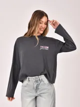 Remera de manga larga color gris oscuro con efecto gastado, corte holgado y estampado frontal con texto en color rosado.