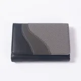 Billetera de cuero sintético y tela, en tonos negro y gris, con diseño de paneles curvos y solapa con cierre.