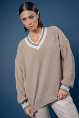 Buzo de punto color beige con escote en V, cuello y puños acanalados con detalles en blanco y azul. Presenta un diseño holgado de manga larga.