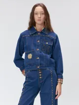 Campera denim crop de mezclilla oscura, con apliques metálicos en el pecho, bolsillos delanteros cruzados con detalles bordados y de parches.