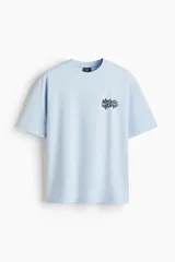 Remera celeste de punto de algodón, de corte holgado con hombros caídos, cuello redondo con ribete acanalado y estampado gráfico en el pecho.