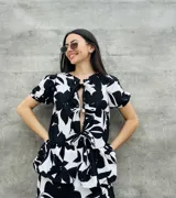 Blusa estampada con hojas verdes y blancas, con escote en V y mangas cortas abullonadas. Presenta volados en el ruedo y detalle de lazos en el frente.