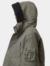 Chaqueta corta tipo bomber con capucha, color verde militar, con cierre frontal de cremallera y botones, bolsillos laterales con solapa y bolsillo utilitario en la manga.