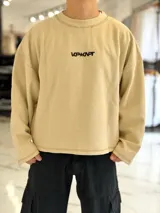 Buzo oversize color beige, con costuras externas visibles y gran estampado tipográfico y gráfico en la espalda.
