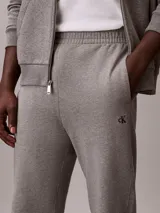 Pantalón jogger gris melange de felpa Calvin Klein, con cintura elástica, bolsillos laterales y puños acanalados. Cuenta con el monograma CK bordado discretamente en la pierna.