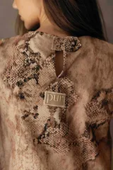 Musculosa de gabardina con estampado de piel de serpiente, cuello redondo y diseño estructurado con abertura en la espalda y ruedo irregular.