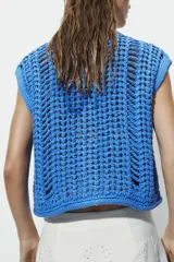 Chaleco azul de punto calado con cuello redondo, sin mangas, cierre frontal con botones y dos bolsillos de parche en la parte delantera.