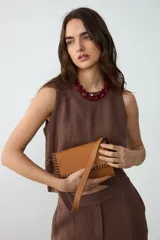Cartera de hombro pequeña de cuero color tostado con detalles de bordado artesanal y costuras en tono chocolate en los bordes y la solapa. Cuenta con correa larga ajustable.