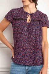 Blusa azul con estampado floral en tonos rosa y celeste, con mangas cortas, cuello redondo con abertura en forma de lágrima y detalle de encaje negro en el pecho.