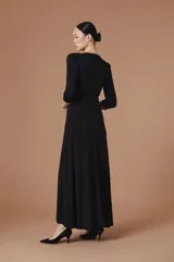 Vestido largo negro de corte elegante con escote en V y mangas tres cuartos. Presenta detalles de pedrería brillante en el borde del escote y en los puños, con un diseño drapeado en la cintura que aporta movimiento y realza la silueta.