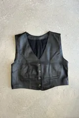 Chaleco negro de cuero napa con forro interior negro, escote en V, cierre frontal con botones y dos bolsillos ribeteados. Confeccionado en Uruguay.