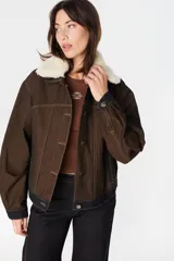 Chaqueta de denim color marrón con costuras en contraste, cuello de lana desmontable en color crema, cierre frontal con botones metálicos y bolsillos laterales.