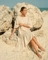 Vestido largo de lino color beige, con mangas abullonadas y volado inferior asimétrico, más largo en la parte trasera.