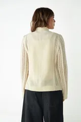 Campera marrón de lana fina sin teñir, con cierre frontal, mangas largas y laterales en tejido de punto. Presenta bolsillos frontales tipo parche.