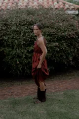 Vestido largo color marrón de crepé plissé, con escote halter adornado con detalles de perlas, silueta fluida y lazo ajustable en la cintura.