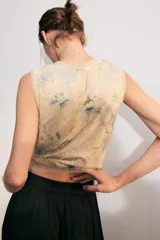Top corto sin mangas, con cuello redondo, confeccionado en tejido de punto cubierto de lentejuelas con estampado floral en tonos azules y verdes sobre fondo beige. Cuenta con cierre en la espalda con abertura y botón.