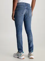 Jeans de hombre, talle bajo, corte slim ajustado, confeccionados en denim azul medio vintage con efecto desgastado. Presentan bragueta con cremallera y diseño de cinco bolsillos.