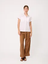 Camisa de manga corta color beige, confeccionada en mezcla de algodón y lino, con cuello camisero, cierre frontal de botones y dos bolsillos aplicados en el pecho.