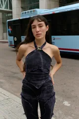 Top halter de denim con efecto lavado, corte entallado y escote alto. Presenta recortes frontales estructurados, terminación desflecada en el frente y un aplique metálico decorativo en el centro del cuello.