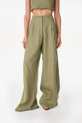 Pantalón de lino blanco de corte ancho y fluido, con cintura alta que incorpora una sobrepretina ancha desmontable con pliegues horizontales.