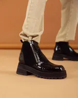 Botinetas negras de caña corta con diseño combinado en cuero charolado con textura de cocodrilo y paneles laterales de gamuza. Presentan cierre lateral metálico, puntera cuadrada y suela de plataforma dentada de goma.