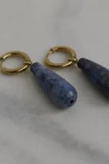 Aros tipo argolla pequeña con dije colgante en forma de gota de piedra natural azul veteada. Realizados en acero quirúrgico dorado.