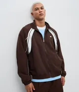 Campera deportiva de poliamida color marrón con detalles en blanco en los hombros y mangas. Presenta cierre frontal completo, cuello alto y puños elásticos.