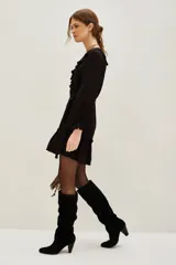 Vestido corto color negro, con escote en V decorado con volados, mangas largas con puños elásticos y falda con volado en el ruedo. Incluye un lazo para ajustar en la cintura.