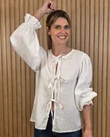 Camisa color beige de lino con mangas abullonadas tres cuartos y cierre frontal mediante múltiples lazos para atar.