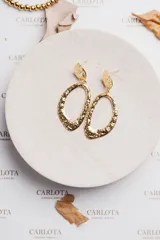 Aros colgantes dorados con forma ovalada irregular y acabado martillado. Fabricados en acero quirúrgico hipoalergénico con baño de oro.