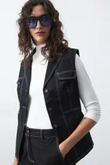 Chaleco sastrero negro con pespuntes blancos a contratono, de inspiración utilitaria. Presenta solapas, cierre frontal con botones y bolsillos delanteros con solapa. Confeccionado en algodón con elastano, ofrece una silueta estructurada y entallada.