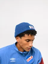 Gorro tipo beanie de punto acanalado en color azul, con parche frontal bordado que incluye el logo de Umbro y la palabra Nacional.