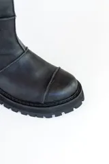Bota de caña media color negro, de cuero, con suela track y cierre lateral.