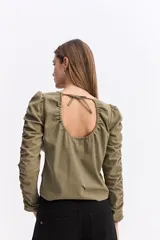 Blusa de manga larga color marrón chocolate, con diseño fruncido central ajustable mediante cordones y mangas con detalle de frunces laterales que aportan volumen.