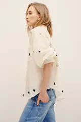 Camisa de algodón color crudo con estampado de corazones negros, de corte holgado, manga larga abullonada y cierre frontal de botones.