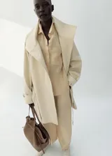 Camisa de lino color beige, de diseño recto con cuello camisero, manga larga con puños abotonados, bolsillo de parche en el pecho y cierre frontal de botones.
