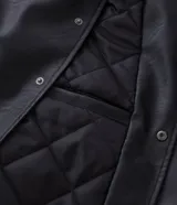 Campera bomber de cuero sintético con diseño bicolor, cuerpo negro y mangas blancas. Presenta cuello, puños y cintura con tejido elástico a rayas, cierre frontal con botones a presión y bordado con la palabra Authentic en el pecho.
