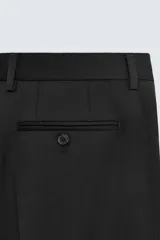 Pantalón de traje regular fit confeccionado en tejido de lana. Presenta bolsillos frontales, bolsillos traseros de vivo con botón y cierre frontal con cremallera y botón.