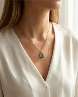 Collar de acero con baño de oro, compuesto por una cadena fina de eslabones y un dije rectangular con una circonia color celeste en el centro.