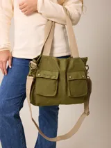 Bolso tipo bandolera de lona color verde oliva, con dos bolsillos frontales con solapa y cierre de broche metálico. Cuenta con correas de hombro y correa larga ajustable en color beige, herrajes metálicos y logo bordado en el frente.