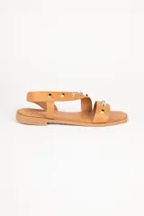 Sandalias bajas de símil cuero color tostado, con tira en diagonal, elástico en el tobillo y detalles de tachas doradas en relieve.