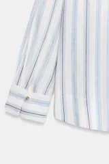 Blusa de manga larga confeccionada en mezcla de viscosa, lino y liocel, con diseño de rayas verticales en tonos celestes y marrones sobre fondo blanco. Presenta cuello solapa con escote en V cruzado.