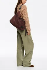 Bolso tipo tote de Bimba y Lola en color marrón, confeccionado en tejido técnico con un bolsillo frontal exterior cubierto por una red decorativa. Cuenta con asas superiores, correa ajustable extraíble y parche con logo de la marca en la parte inferior.