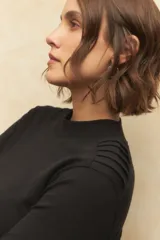 Polera de manga larga en color negro, confeccionada en algodón, con cuello alto y detalle de frunces en los hombros.